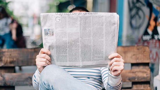 A man sitting on a bench with a newspaper covering his face.
