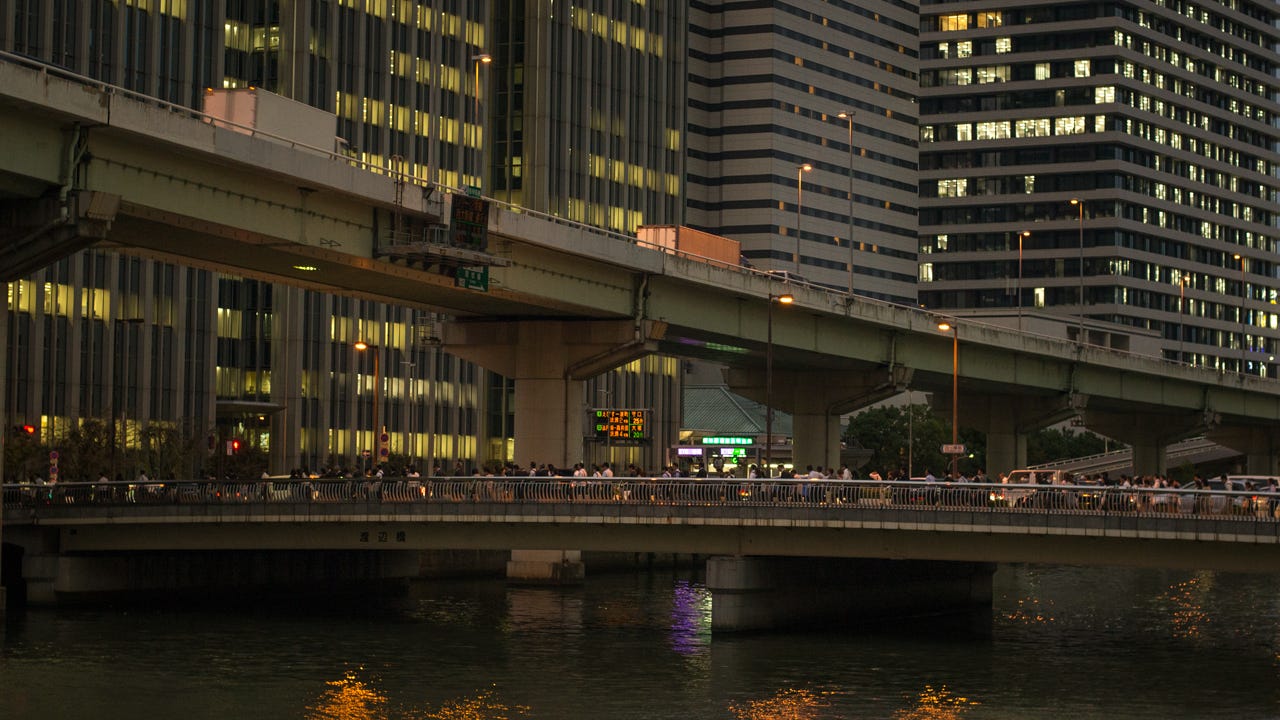 A wall of office buildings and a bridge with office workers walking across in Osaka, Japan.